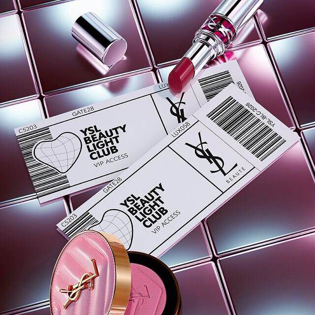 Prodotti di bellezza YSL (rossetto e fard) disposti con biglietti d'accesso VIP su una superficie metallica riflettente.