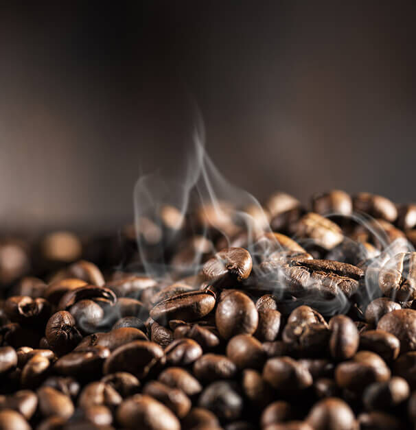 A close-up of freshly roasted coffee beans with wisps of steam rising, set against a dark background.