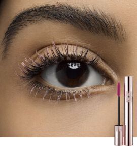 Close-up of an eye with long, defined lashes, featuring a tube of mascara and a pink lip product beside it.