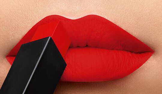 Close-up of a pair of lips painted in vibrant red lipstick, with a lipstick tube being applied directly to the lips.