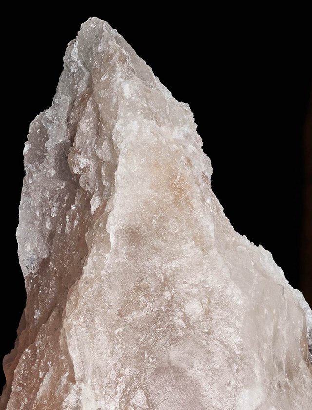 A close-up of a jagged, crystal-like formation with a pointed tip, illuminated against a dark background.