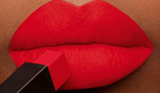 Close-up of bold red lips with a lipstick bullet positioned just above them.