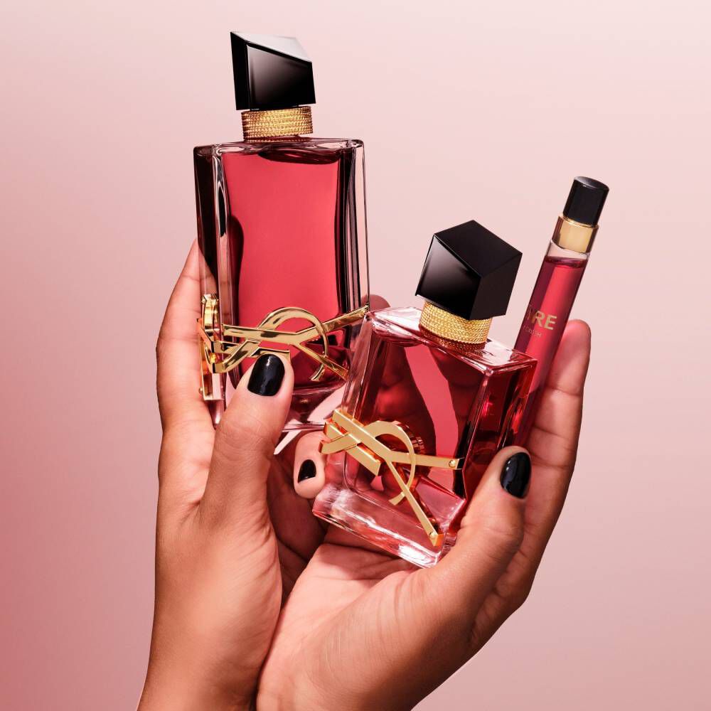 Mani che tengono due flaconi di profumo YSL rossi e uno spray da viaggio