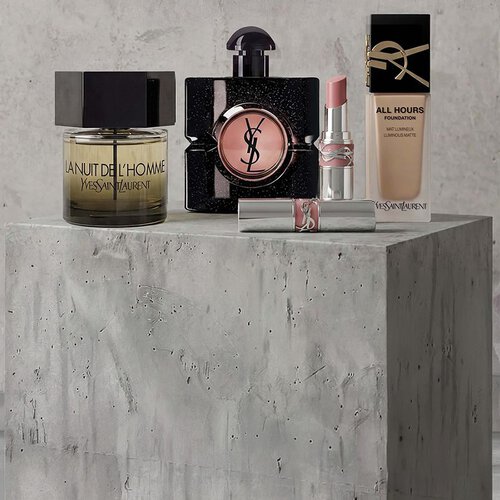 Presentazione promozionale di prodotti di trucco YSL Beaute tra cui mascara, una palette di ombretti trapuntata e rossetti su sfondo in cemento.