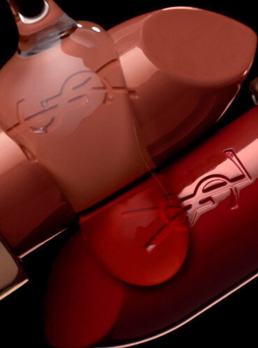 A close-up of several elegant lipstick tubes in varying shades of nude and red, featuring the YSL logo prominently on their surfaces, against a dark background.