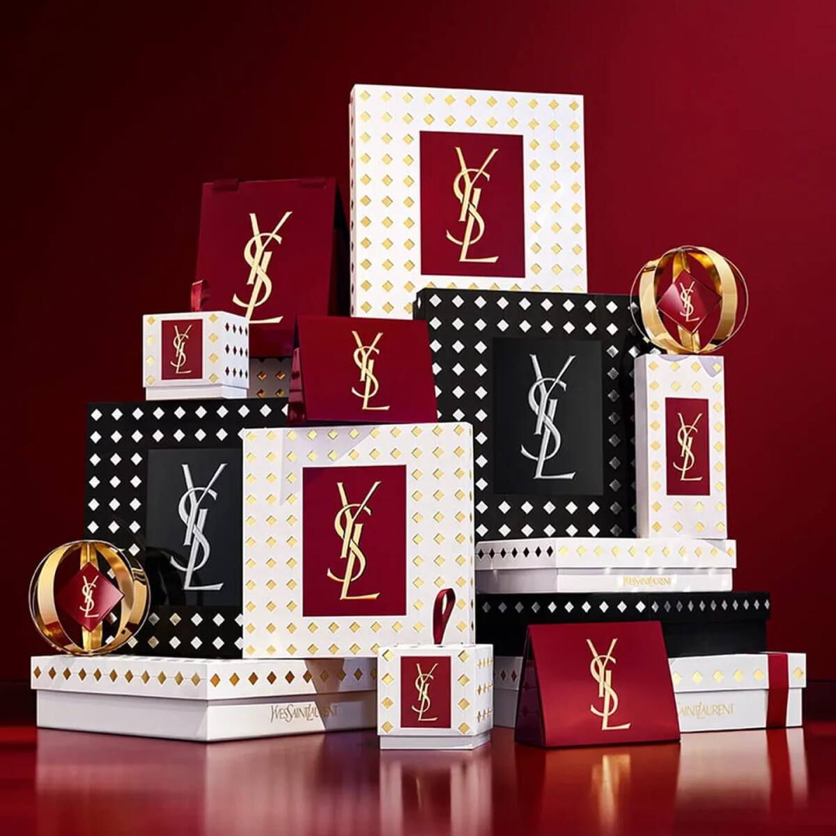 Cofanetti regalo della collezione natalizia Yves Saint Laurent e prodotti di bellezza di lusso su sfondo rosso festivo.