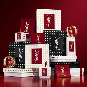 Cofanetti regalo della collezione natalizia Yves Saint Laurent e prodotti di bellezza di lusso su sfondo rosso festivo.