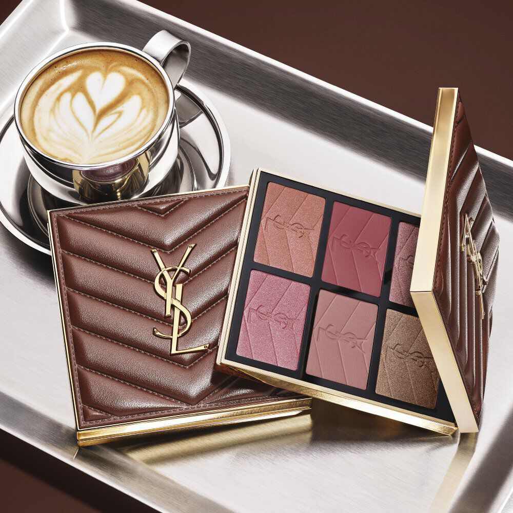 Palette trucco YSL e pochette matelasse accanto a un caffe su un vassoio argentato.