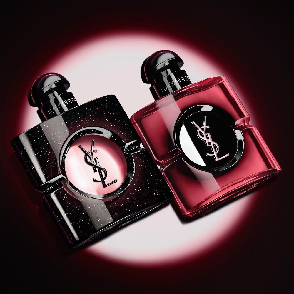 Due flaconi di profumo Black Opium di Yves Saint Laurent illuminati su sfondo scuro.