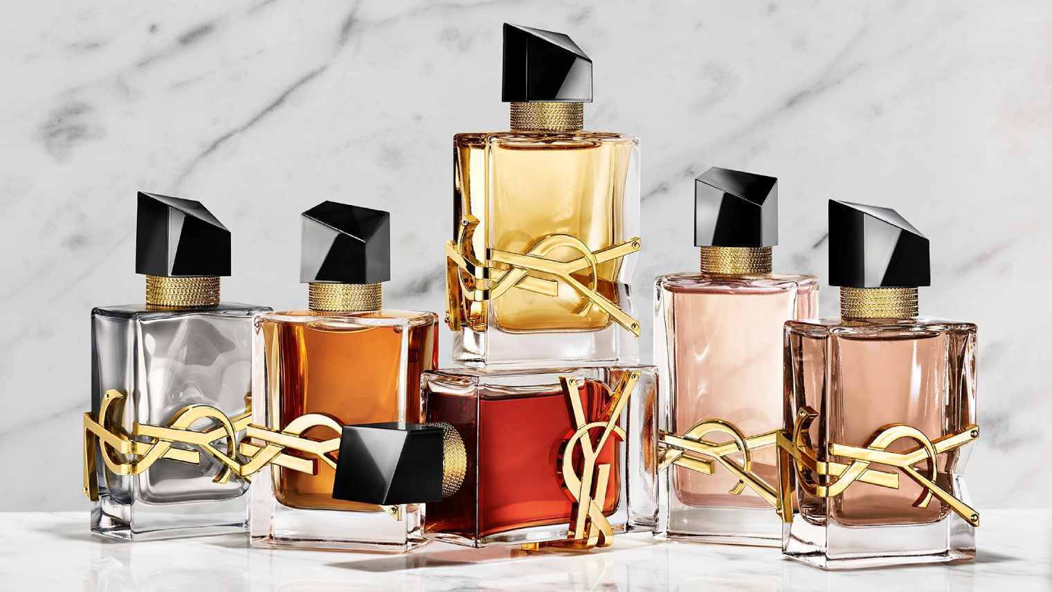Una mano tiene un flacone di profumo YSL rosso accanto ad altre due fragranze su una base di pietra.