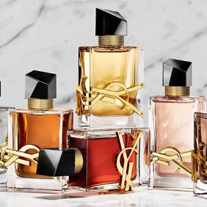 Una mano tiene un flacone di profumo YSL rosso accanto ad altre due fragranze su una base di pietra.