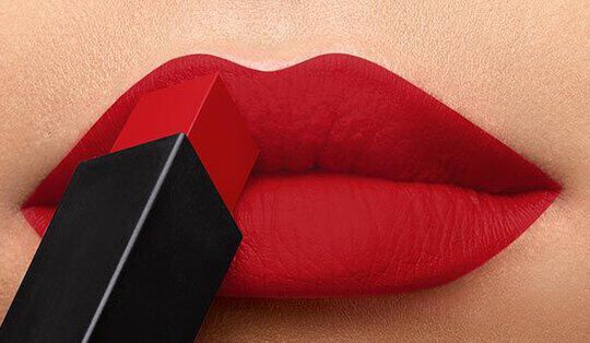 Close-up of a woman's lips coated in bright red lipstick, with a red and black lipstick tube poised above.