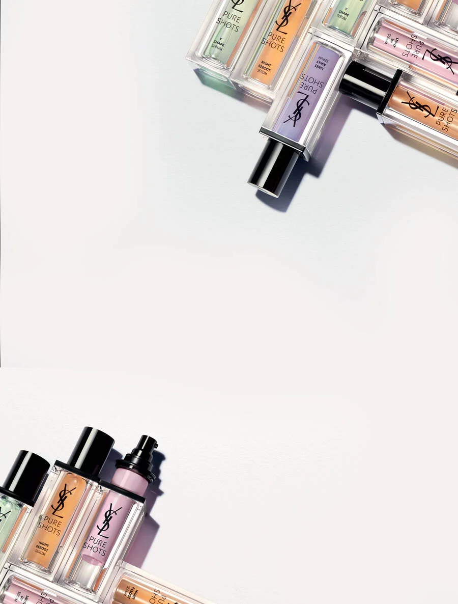 A flat lay of various YSL beauty products, including bottles of foundation and other makeup items, arranged artistically on a light background.