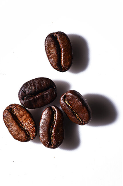 Five roasted coffee beans arranged on a white background, casting subtle shadows.