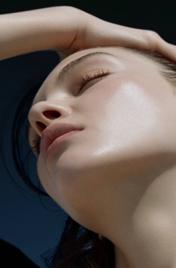 A close-up of a woman's face with radiant skin, angled slightly upward, capturing a serene expression.