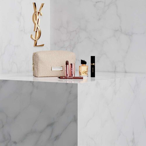 Pochette, profumo Libre e prodotti make-up YSL su fondo in marmo bianco.