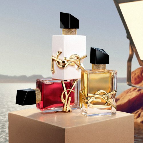 Flaconi di profumo YSL disposti su un piedistallo davanti a un paesaggio desertico.