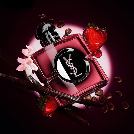 Flacone di profumo YSL Black Opium circondato da chicchi di caffe, fragole, bacche di vaniglia e fiori bianchi su sfondo scuro.