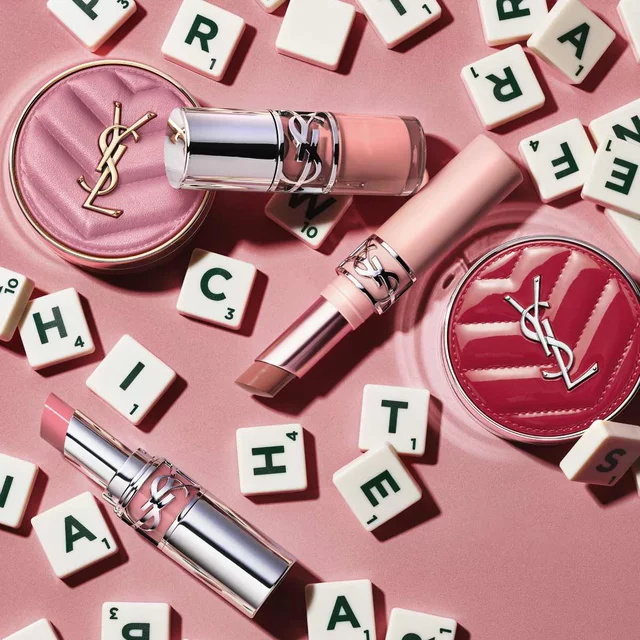 Prodotti make-up YSL e tessere con lettere su sfondo rosa.