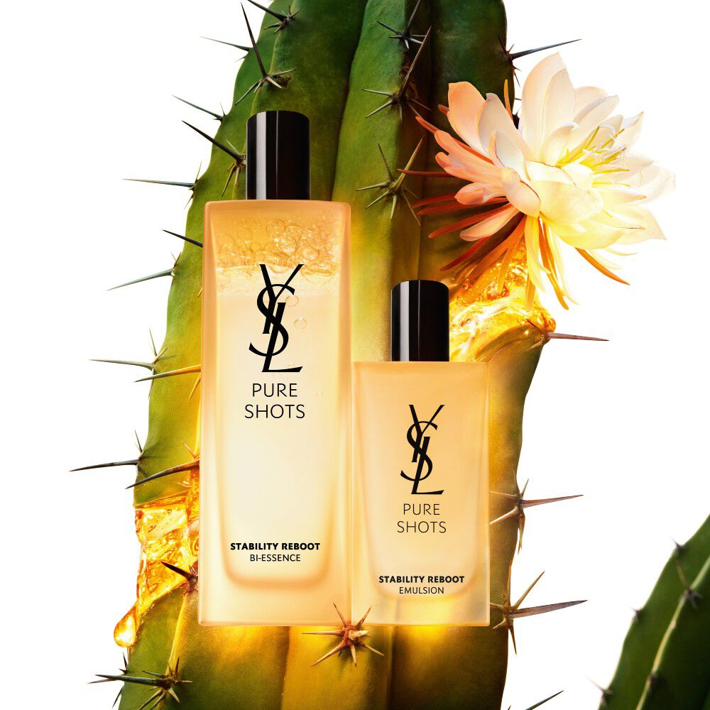 Due prodotti per la cura della pelle YSL Pure Shots, un bi-essence e un'emulsione, su uno sfondo di cactus con un fiore bianco in fiore.