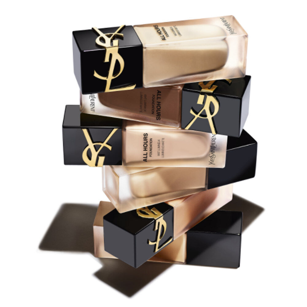 A stack of YSL All Hours foundation bottles in various shades, with sleek black and gold packaging.