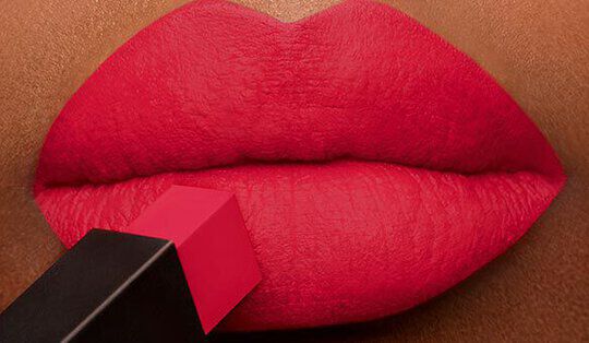 Close-up of full, red lips with a lipstick tube poised above, emphasizing a bold makeup look.