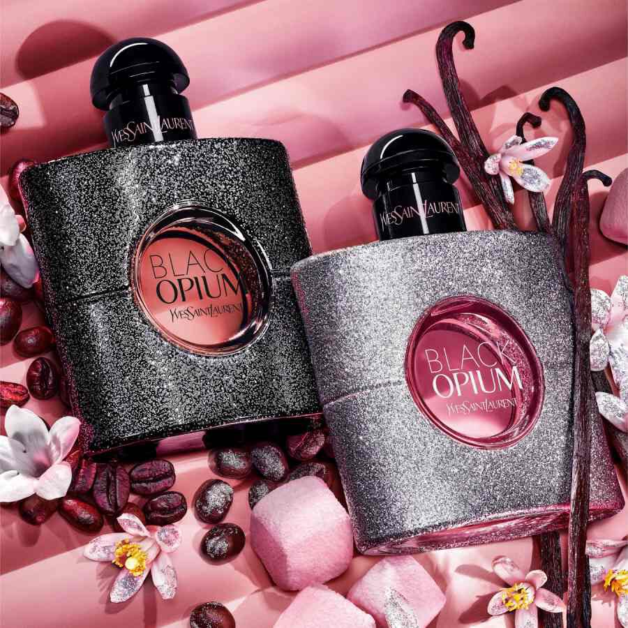 Due flaconi YSL Black Opium su sfondo rosa con fiori e chicchi di caffe