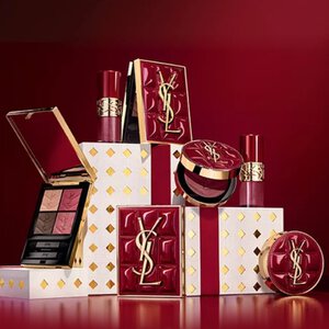 Cofanetti regalo della collezione natalizia Yves Saint Laurent e prodotti di bellezza di lusso su sfondo rosso festivo.