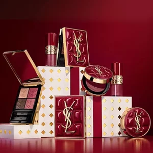 Cofanetti regalo della collezione natalizia Yves Saint Laurent e prodotti di bellezza di lusso su sfondo rosso festivo.