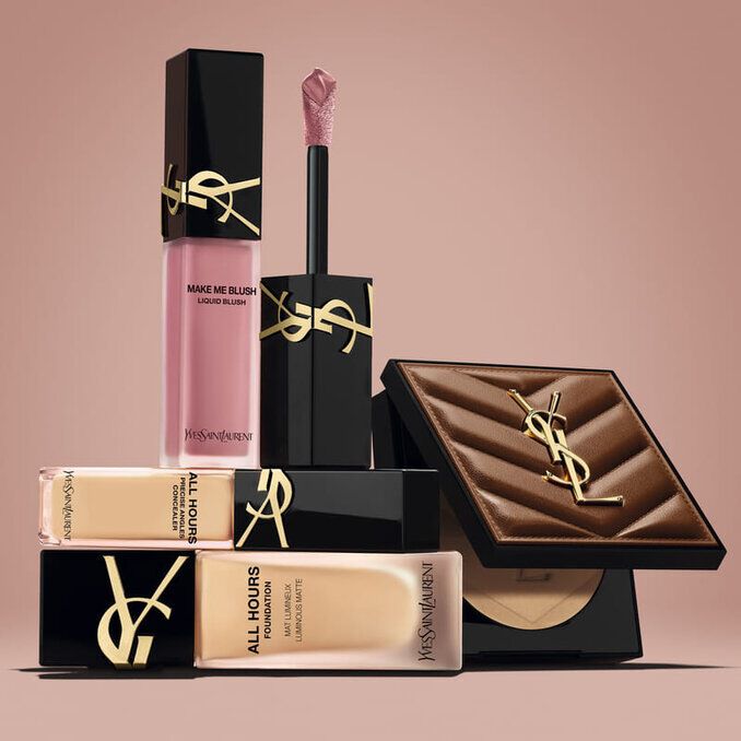 Prodotti beauty YSL, tra cui blush, fondotinta e cipria compatta, su sfondo nude.