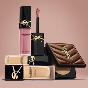 Prodotti beauty YSL, tra cui blush, fondotinta e cipria compatta, su sfondo nude.
