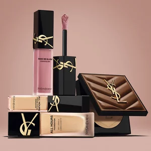 Prodotti beauty YSL, tra cui blush, fondotinta e cipria compatta, su sfondo nude.