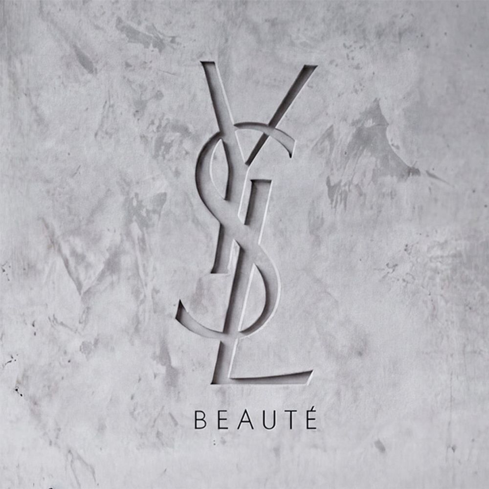 Logo YSL BEAUTE inciso su una parete in cemento grigio strutturato.