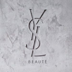 Logo YSL BEAUTE inciso su una parete in cemento grigio strutturato.