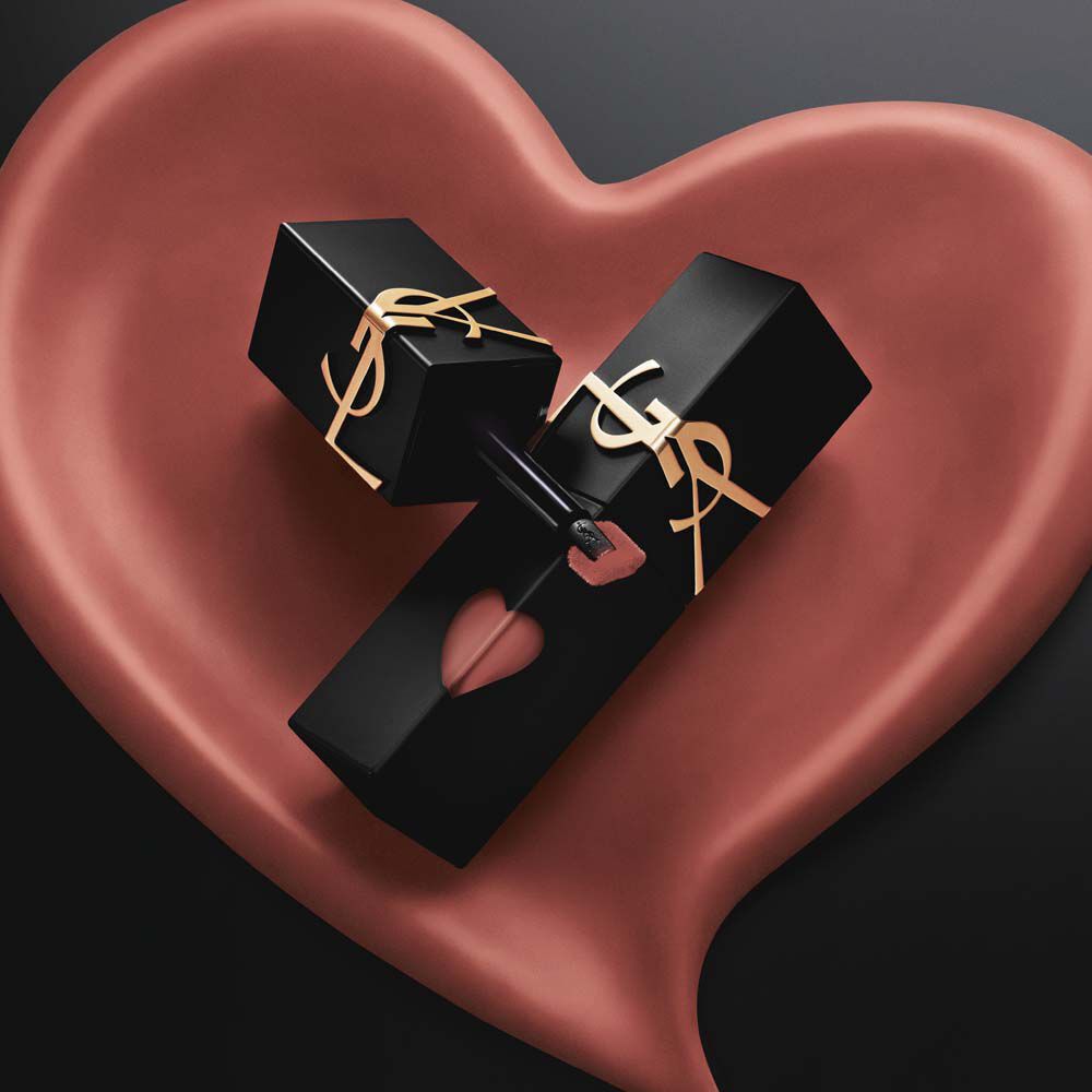 Due laccetti YSL in nero opaco, con cuori rosa intagliati e loghi dorati, esposti dentro un cuore scolpito in rosa opaco abbinato, su sfondo nero.