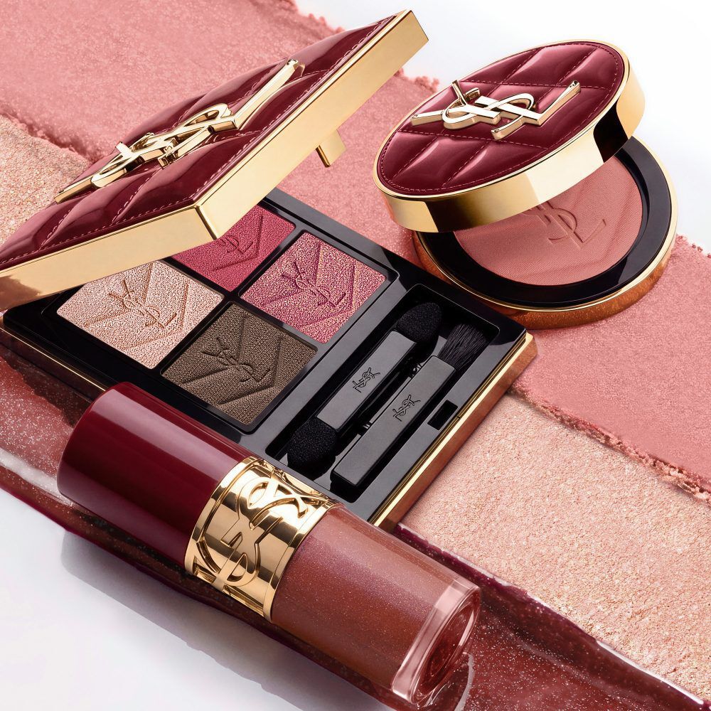 Modella in completo nero e look glamour, seduta in un’atmosfera festiva illuminata dalle candele, circondata da cofanetti regalo YSL.