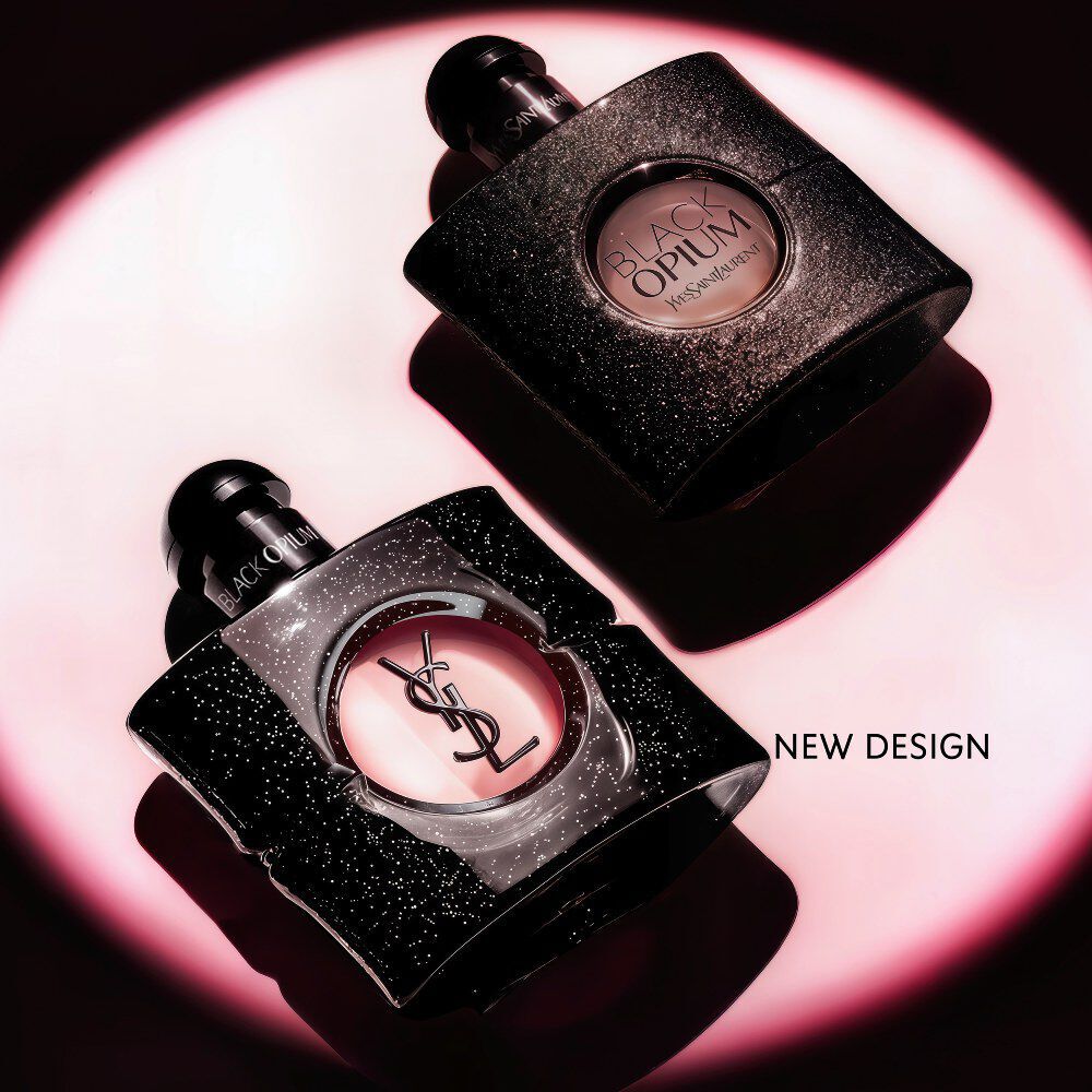 Flacone di Black Opium Eau de Parfum adagiato su un fianco su una superficie scura, avvolto da un alone di luce rosa.