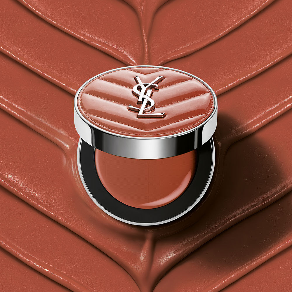 Un astuccio aperto di YSL Make Me Blush Lifted Glow Cream Blush nella tonalita #44 Nude Lavalliere su uno sfondo crema testurizzato rosa abbinato.