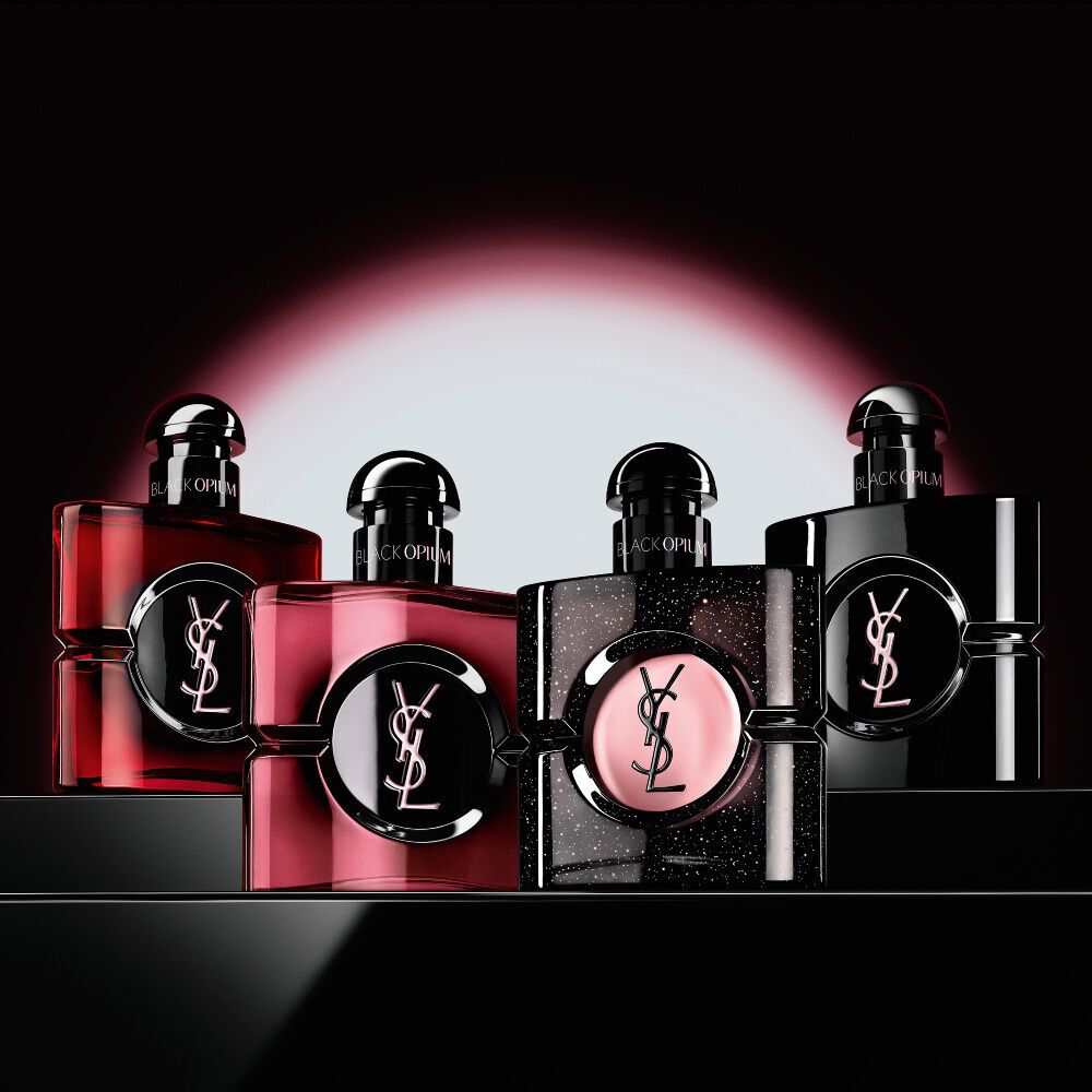 Quattro diversi flaconi di profumo Black Opium esposti in fila su una superficie scura e riflettente.