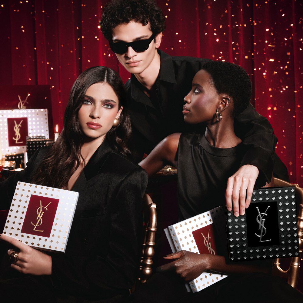 Modelle unite in posa, mani che stringono i lussuosi cofanetti regalo YSL Holiday, atmosfera festiva.