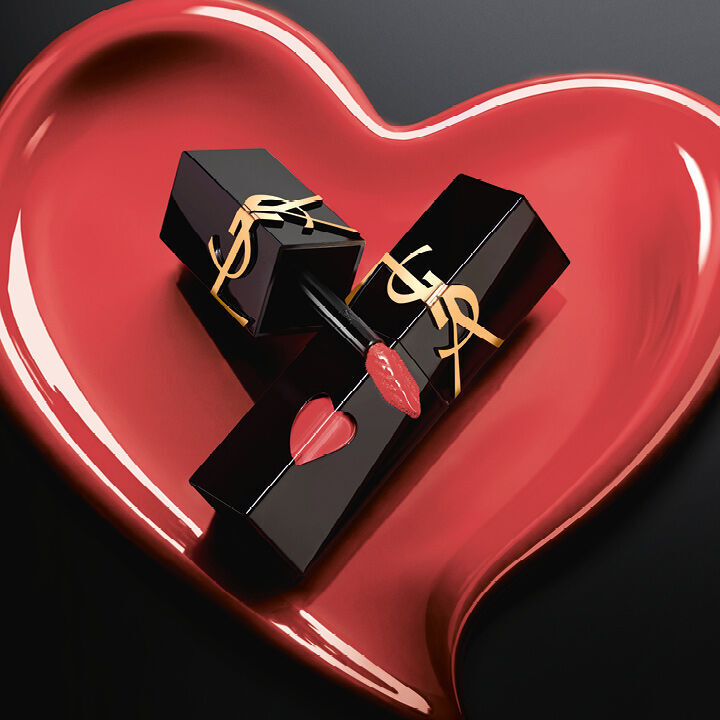 Due laccetti opachi neri YSL con taglio a cuore rosa e logo dorato, esposti in un cuore scolpito opaco rosa abbinato su sfondo nero.