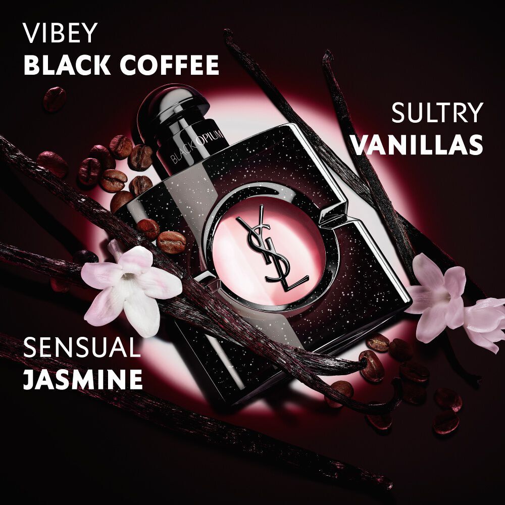 Primo piano di chicchi di caffe tostati, bacche di vaniglia e fiori di gelsomino disposti attorno all’iconico flacone di Black Opium Eau de Parfum con la Cassandre YSL.