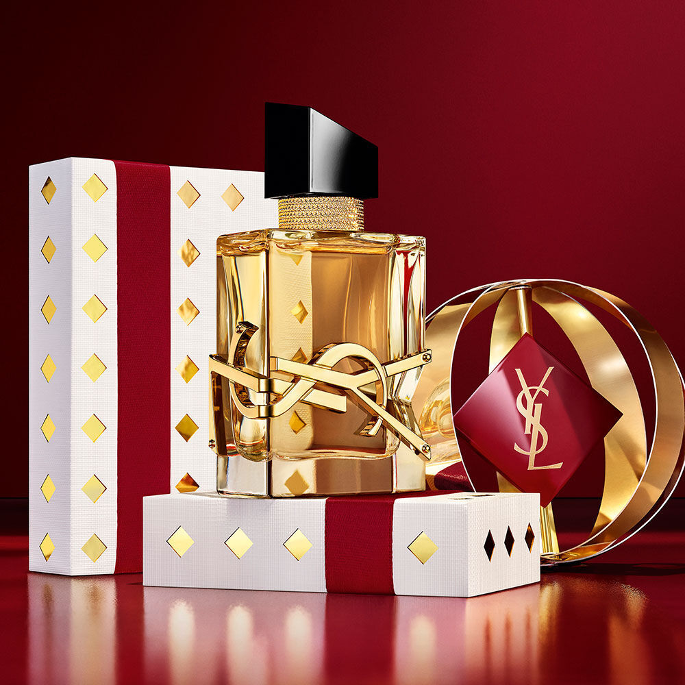 Flacone iconico di LIBRE in primo piano, tra cofanetti regalo YSL in borgogna e oro di lusso.