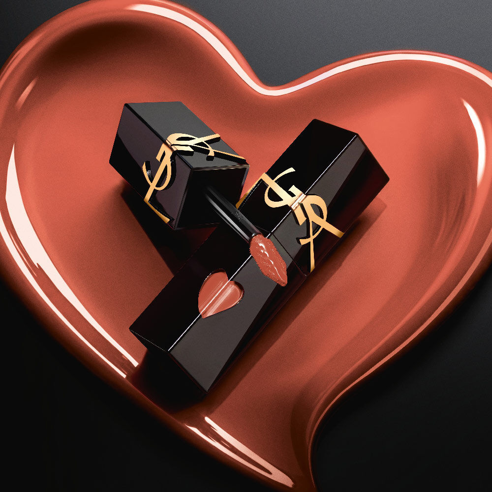 Due laccetti opachi neri YSL con taglio a cuore rosa e logo dorato, esposti in un cuore scolpito opaco rosa abbinato su sfondo nero.