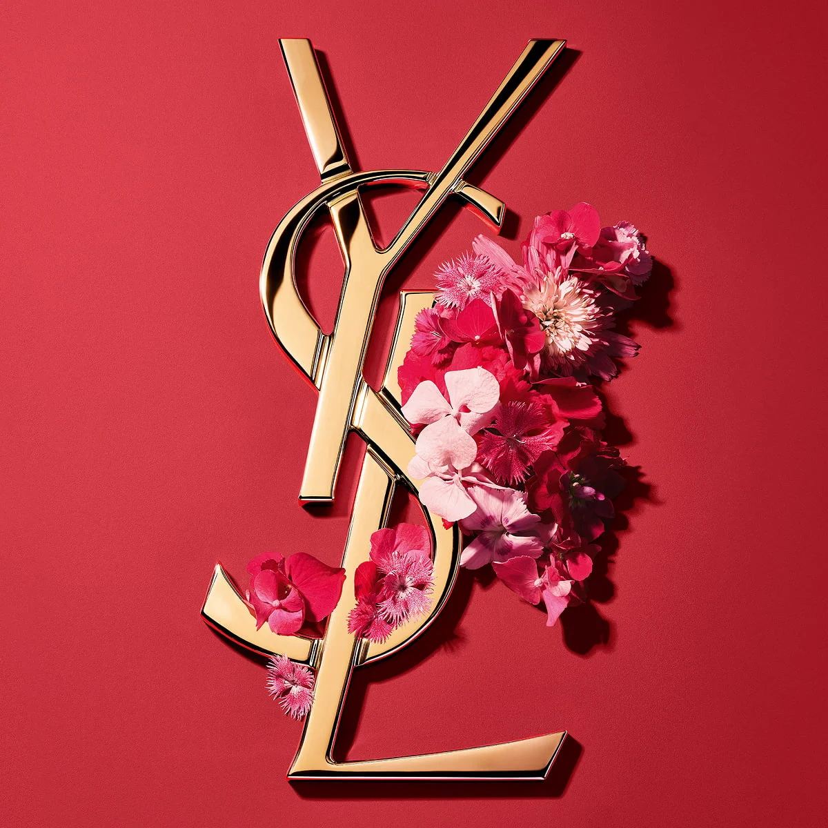 Logo Cassandre dorato YSL, ornato con vibranti fiori primaverili rosa, su uno sfondo rosa.