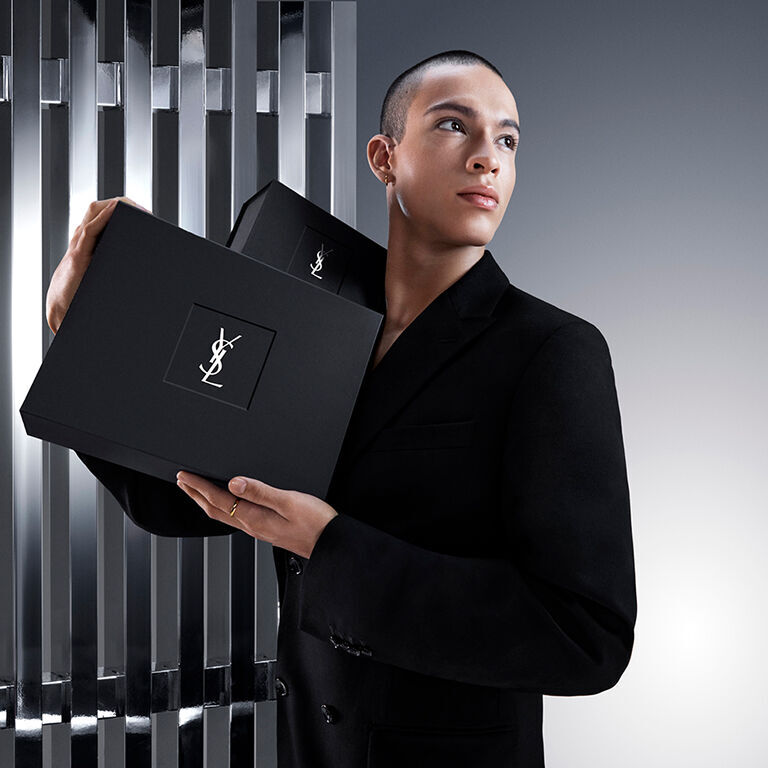 Pierre-Antoine, un modello, tiene con eleganza un'elegante confezione regalo nera YSL Beauty con l'iconico logo Cassandre.