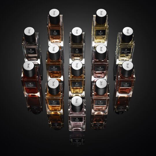 Una collezione di flaconi di profumo YSL disposti su una superficie scura riflettente.