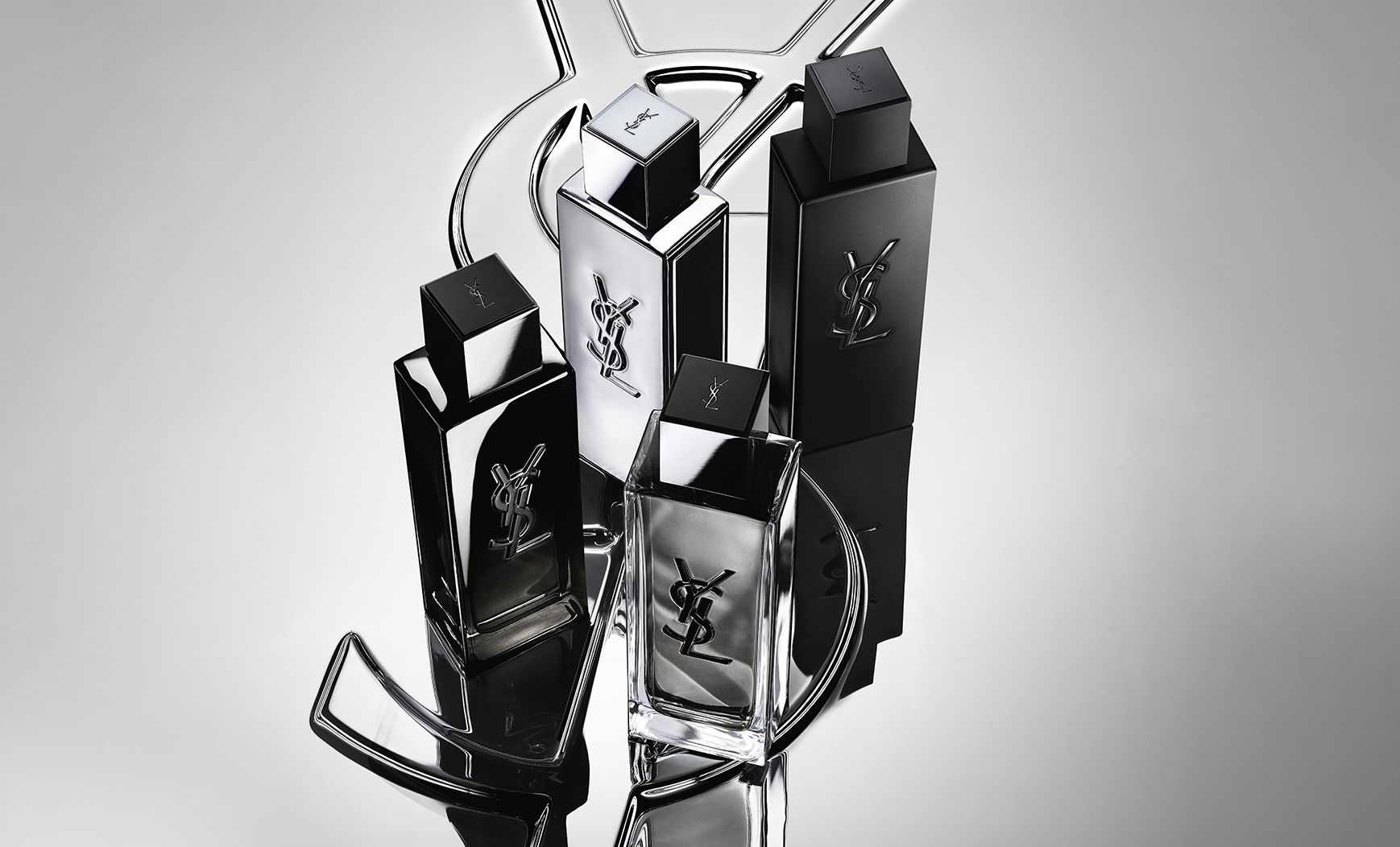 Scatto di gruppo dell'intera gamma di fragranze MYSLF, con i flaconi posizionati su un grande logo Cassandre YSL con effetto specchio riflettente.