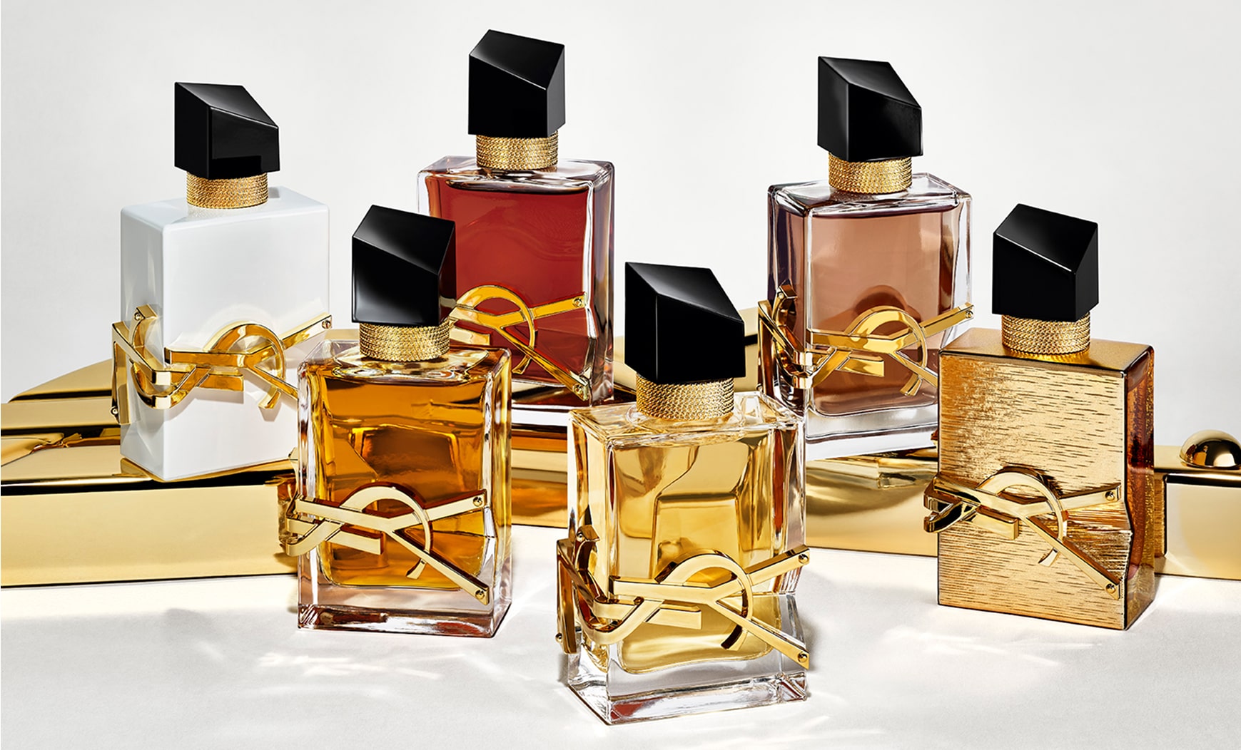 Due fragranze del profumo YSL Libre esposte su una superficie dorata lucida. I frasco variano nel colore del liquido e nella finitura del flacone, includendo tonalità trasparenti, bianche, rosse e marroni, e un frasco dalla texture completamente dorata. Tutti presentano le iconiche lettere YSL in oro e un carattere nero inclinato.


