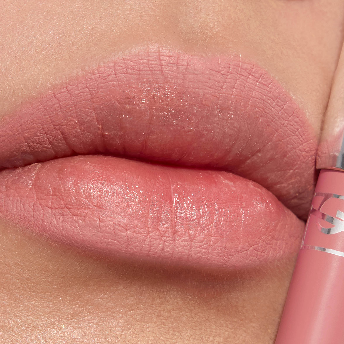 Primo piano di labbra con un rossetto opaco rosa tenue e il relativo tubetto.